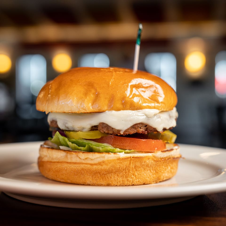 A Kely's Crepes & Burgers cheeseburger with lettuce, tomato, and pickles on a white plate.