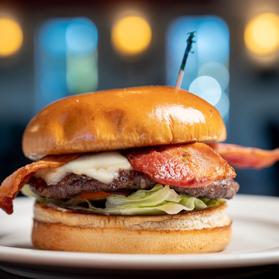 Kely's Crepes & Burgers' bacon cheeseburger with lettuce and tomato on a white plate.